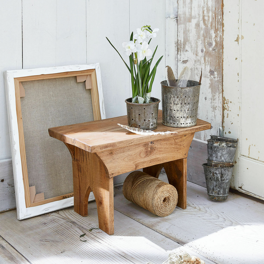 Kleiner Holzschemel mit Metalltöpfen und weißen Blumen auf hellem Holzboden
